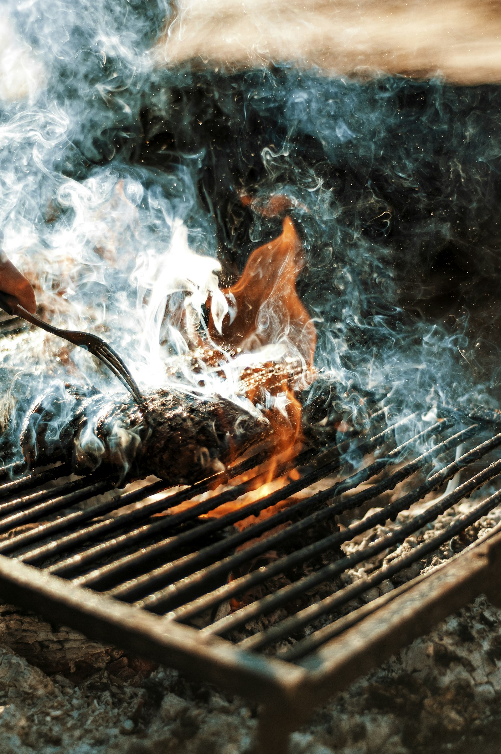 Humo levantándose de la parrilla mientras se voltea un corte sobre la brasa